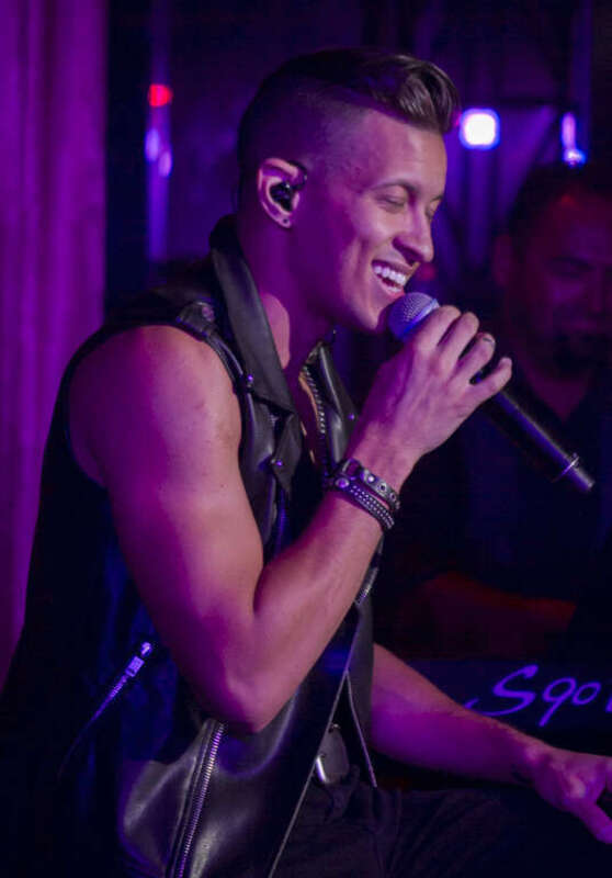 Chaz Robinson, a man, singing while seated, wearing a leather vest, and smiling.