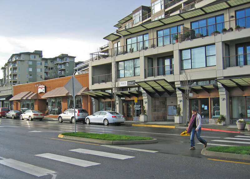 Pedestrian crosses street using yellow pedestrian flag in downtown Kirkland. Note how cross walk shifts at a angle in the median.  This shift forces pedestrians to look at on coming traffic.  Mix-use development adds to walkable environment.
This