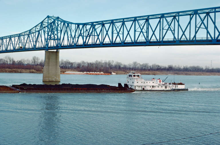 Looking NNE from Kentucky bank.
Towboat &quot;Olmstead&quot; (doc. # 624201) downbound at Glover Cary Bridge (opened to traffic in 1940).
Ohio River mile 756.
Owensboro, Kentucky.
Dec. 1987.
File # 87l032.
.
&quot;Olmstead&quot; was built in 1980 by St. Louis Ship and