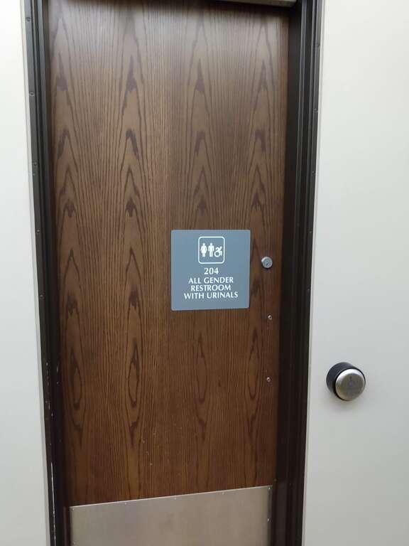 A sign on a door for an All Gender Restroom with Urinals in the University Center at the University of Montana.