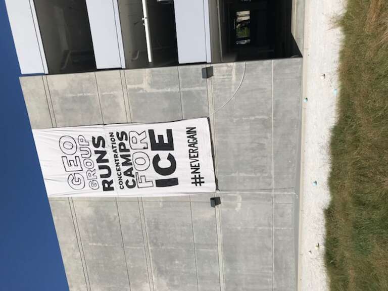 Sign hoisted by #Never Again during protest outside GEO Group's Century City office building in Los Angeles. (8/05/19)
