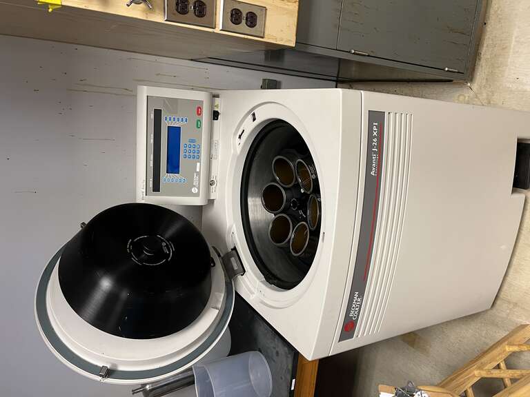 A centrifuge with its lid open inside a lab room.