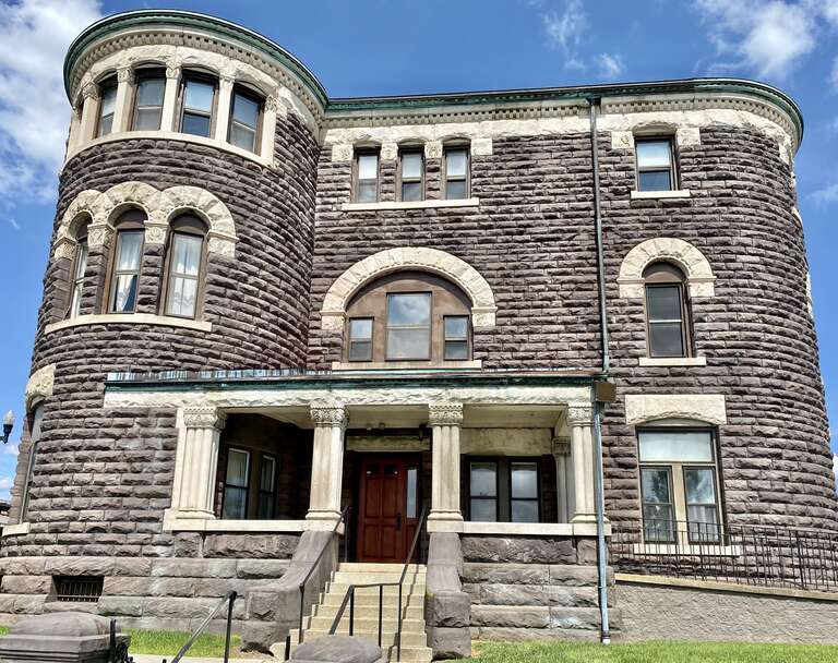 Built in 1889, this Richardsonian Romanesque Revival-style building was designed by Joseph W. Yost to serve as the jail and Sheriff’s residence for Licking County, Ohio.  The building features a rusticated brownstone exterior with limestone trim, a