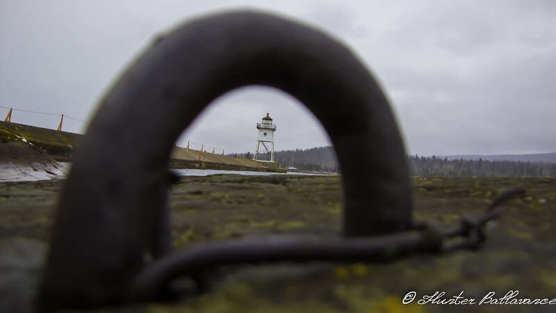500px provided description: a picture of a light house through a boat tie down [#water ,#boat ,#travel ,#light ,#lighthouse ,#fishing ,#tiedown ,#grand marais lighthouse]
