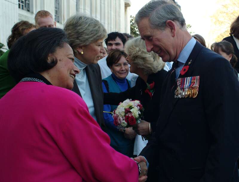 Group of figures outdoors; in the foreground, Karen Hastie Williams and Charles, Prince of Wales, shake hands.