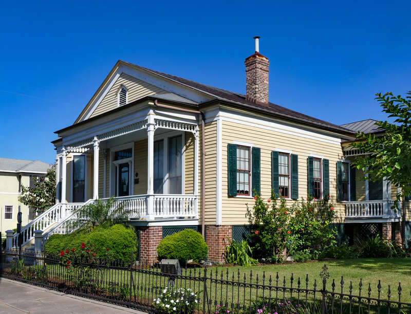 The Quigg-Baulard Cottage was originally built by William and Josephine Quigg in 1867. The wooden house with clapboard siding includes five-foot brick piers. The front exhibits Greek revival features, characteristic of mid-19th century Galveston. A