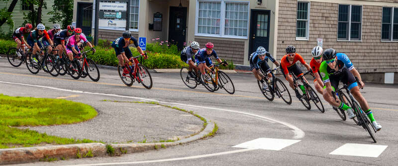 These bikers are finishing the last lap of the Yarmouth Clam Festival bicycle race in Yarmouth, Maine.  It was very hot and humid on this race day.   These were not the leaders but I liked the long line of bikes leaning into a very sharp turn into a