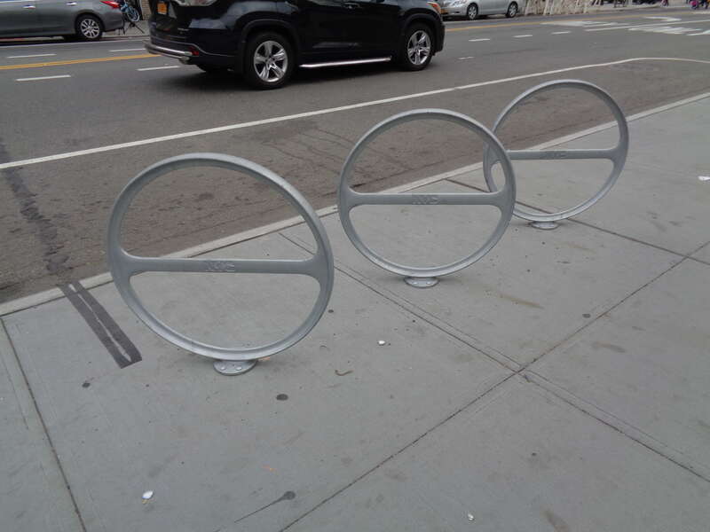 Modern municipal bicycle racks at the east end of the Nine Heroes Plaza / Vietnam Veterans Triangle, on the south side of Broadway at 76th Street and 41st Avenue in Elmhurst, Queens.