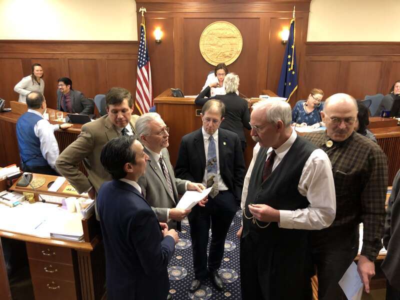 A group of senators huddling in the Senate chamber on a piece of legislation.