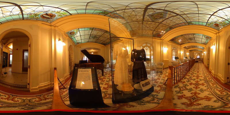 Ornate stained glass and colorful tile floors adorn this assembly room. A baby grand piano sits in the distance next to a display case featuring historical garments.
This is on the 3rd floor of the Bathhouse. The Assembly Room features an original