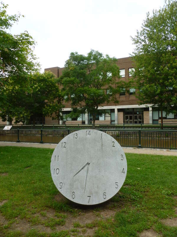 The front side of a 14 hour clock monument at Lucy Larcom Park, made by Ellen Rothenberg in 1996.  The work memorializes the &quot;10 hour movement&quot; of the early 1800's, spearheaded by female workers in Lowell.  
An inscription that circles along the