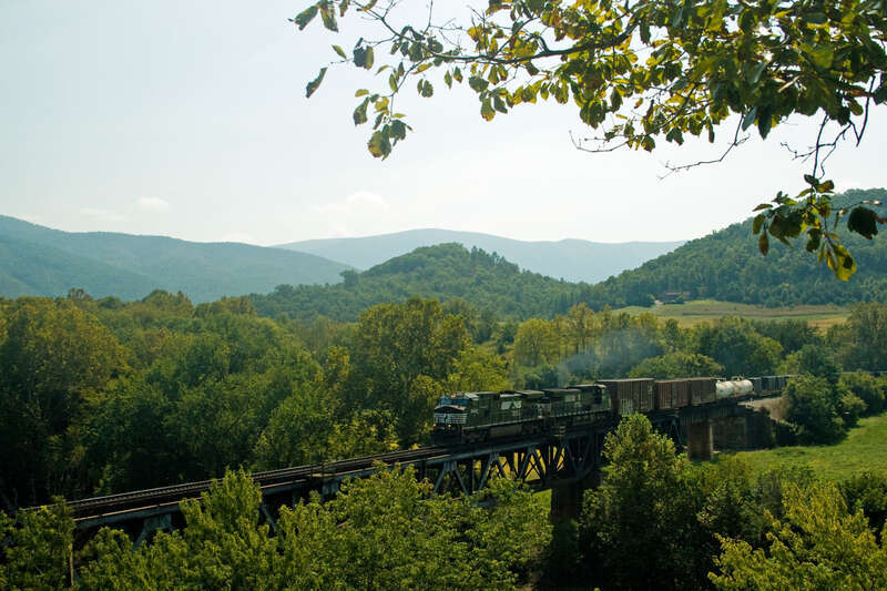 The beauty of the Blue Ridge Mountains in VA is enhanced by a NS manifest train.  This picture was taken in Natural Bridge Station, VA.  Here the NS crosses the James River and then the CSX James River line.  A nearby landowner has cleared the bluff