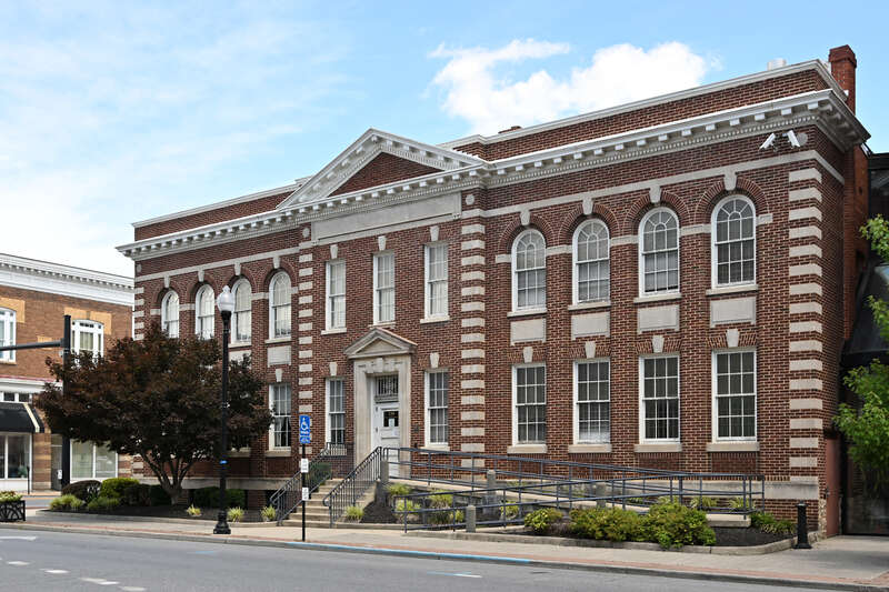 A two story brick building with stairs and a ramp leading up to the front door. This building is used by the Jefferson County Circuit Clerk. 19 North George Street, Charles Town, West Virginia, 25414.