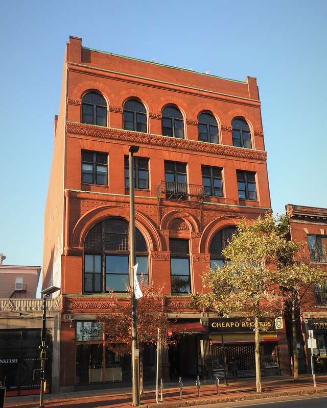 Looking southwest across Massachusetts Avenue on a sunny morning at building having a record shop and dance studios.