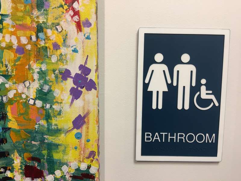 A sign indicating a gender-inclusive, ADA compliant restroom at a public library in Nashua, New Hampshire