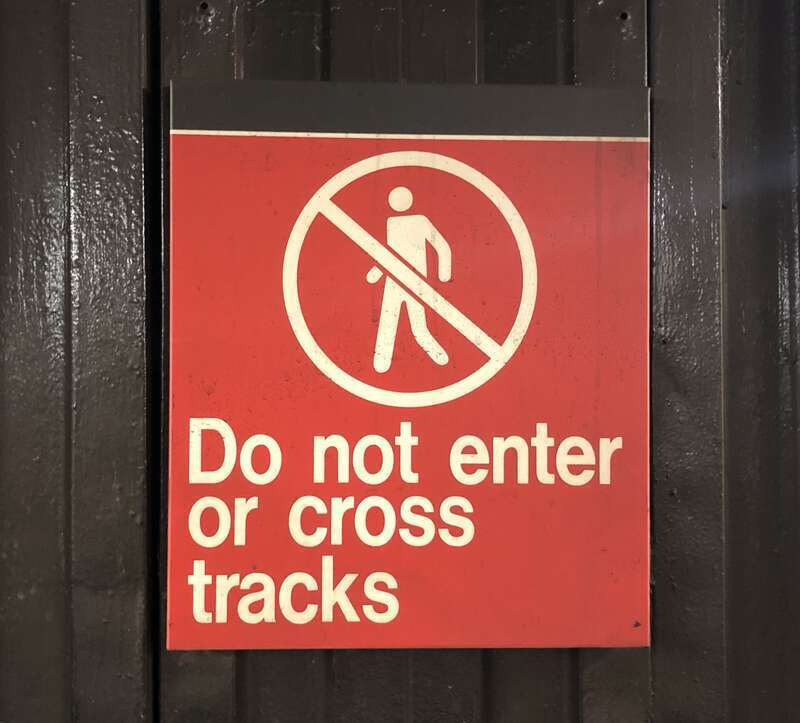 This is an image of a sign near one of the ends of a New York City Subway platform, serving to warn passengers not to enter or cross the tracks.