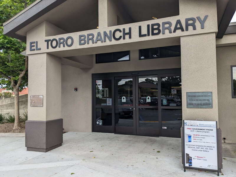 The front entrance of the El Toro Branch Library, a public library with the Orange County Public Library system in Lake Forest, Orange County, California. Legible information includes the name of the library, information about receiving a free phone