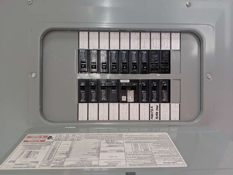 An electrical breaker panel. The switches are labeled according to which circuit breaker they control. Warnings are seen on this inside of the door.