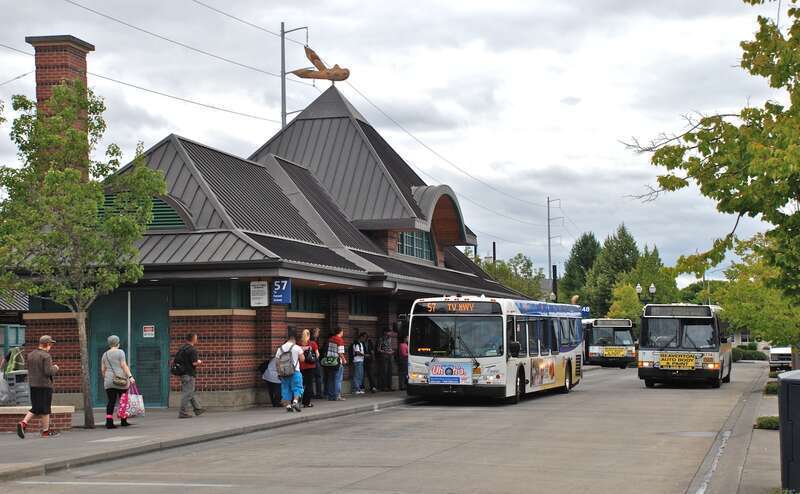 The north side of TriMet's Hillsboro Transit Center during rush hour, with passengers waiting to board a westbound line 57-TV Highway bus. Another bus is arriving on line 47, and a third bus is laying over on line 48.  On the opposite side of the