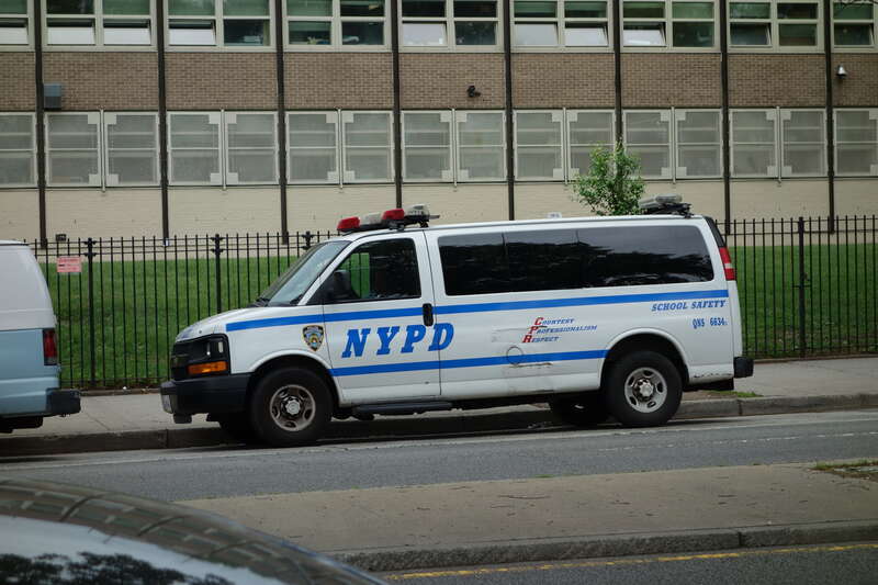 Looking east across Main Street at John Bowne High School south of 63rd Avenue / Reeves Avenue in Queensboro Hill / Kew Gardens Hills, Flushing, Queens. Pictured is an NYPD school safety van.