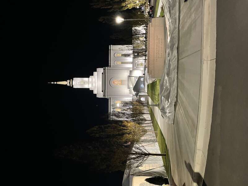 A picture of the Orem Utah Temple at night. Garden elements can be seen in the foreground, plastic wrapping shows underneath a sign that says: &quot;The Church of Jesus Christ of Latter Day Saints, Orem Utah Temple.&quot;