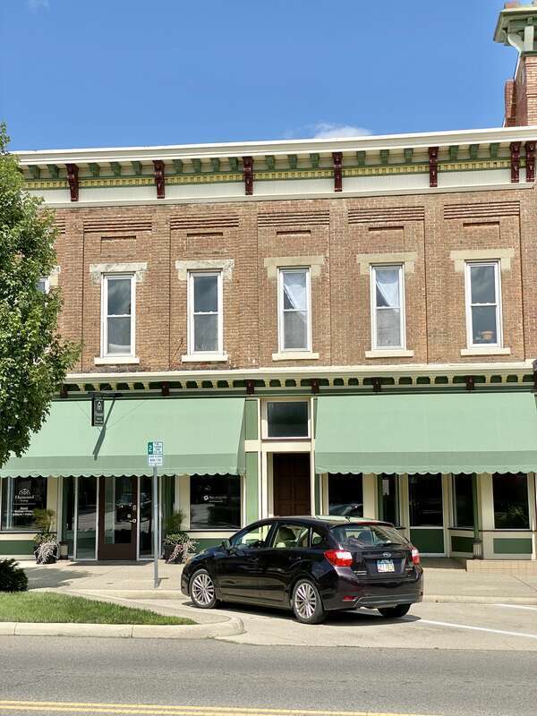 Built in the late 19th Century, this Italianate-style building features a red brick facade with a bracketed cornice featuring modillions and dentils, stone lintels and sills, pilasters between the window bays with recessed brick panels and brick