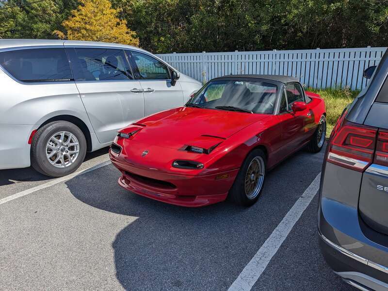 A red Mazda Miata (NA) with aftermarket headlights parked outside the Brevard Zoo in Viera, FL