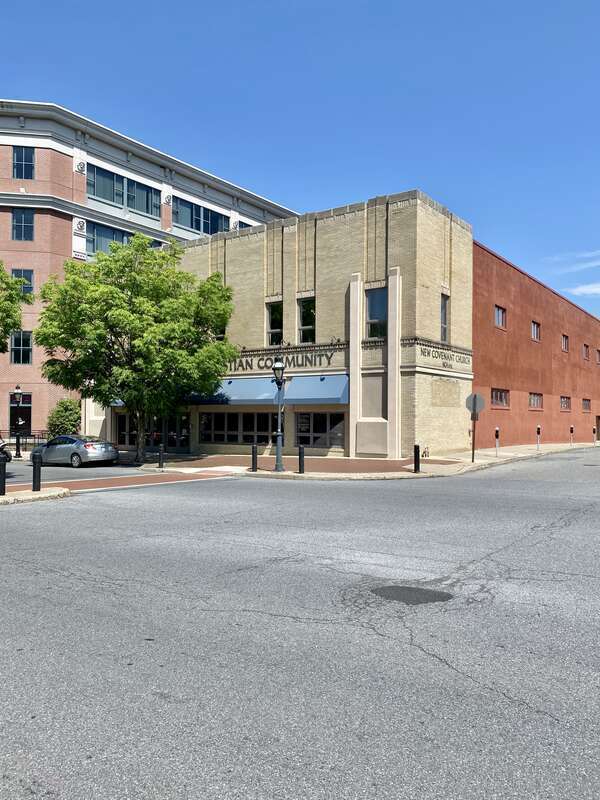 Built in the early 20th Century, this Art Deco-style building features a buff brick front facade and stucco-clad sides, stone trim, recessed panels above the window openings, decorative trim above the windows and below the parapet cap, decorative