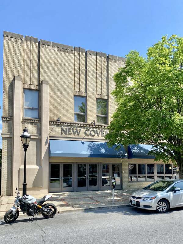 Built in the early 20th Century, this Art Deco-style building features a buff brick front facade and stucco-clad sides, stone trim, recessed panels above the window openings, decorative trim above the windows and below the parapet cap, decorative