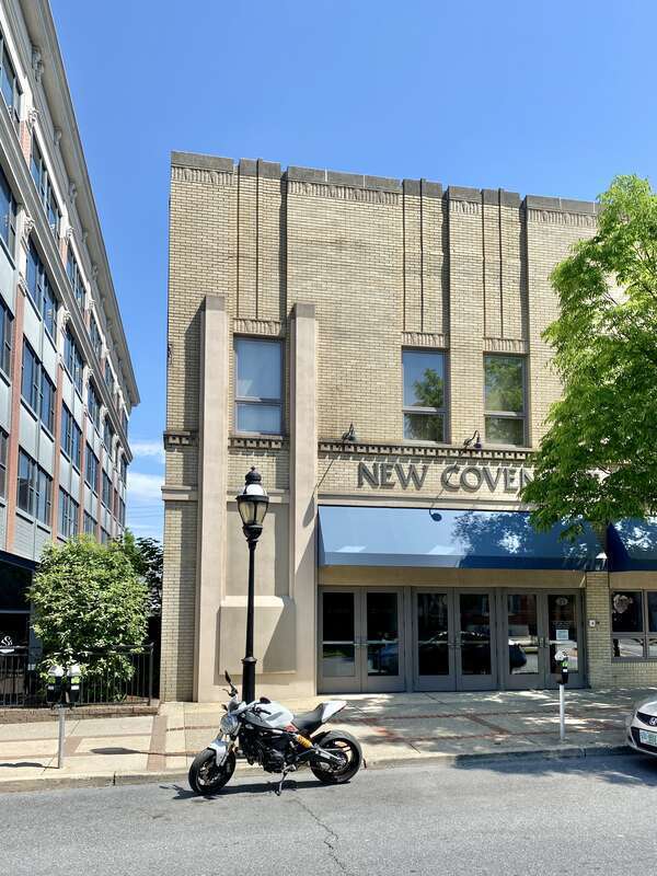 Built in the early 20th Century, this Art Deco-style building features a buff brick front facade and stucco-clad sides, stone trim, recessed panels above the window openings, decorative trim above the windows and below the parapet cap, decorative