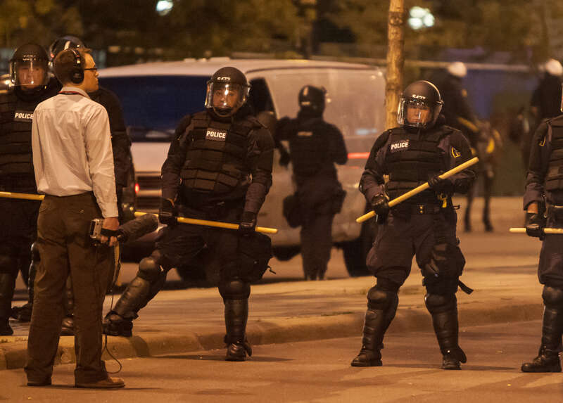 A reporter records audio along a line of police in riot gear at the 2008 Republican National Convention in Saint Paul, Minnesota