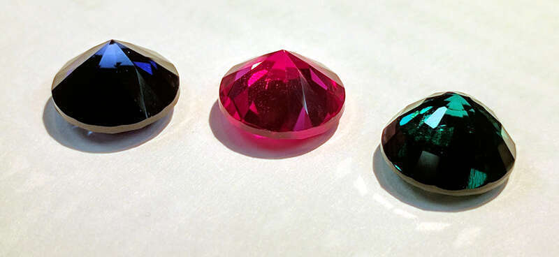 A set of synthetic 9mm round cut gemstones: a sapphire, a ruby and an emerald. The emerald was produced using the hydrothermal process; the sapphire and ruby by the flame fusion aka Verneuil process.