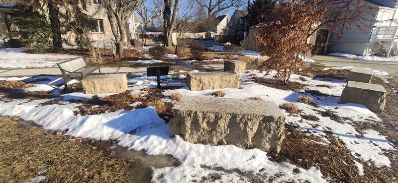 A small parklet in Wauwatosa, WI in winter with some small benches and a sign
