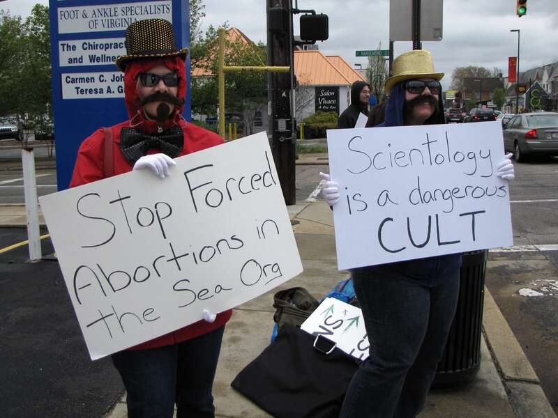 Arcadia and HT, from the Washington DC Anonymous cell, at the Church of Scientology mission in Richmond, Virginia.  Arcadia holds a sign saying, &quot;Stop Forced Abortions in the Sea Org&quot;, and HT holds one that says &quot;Scientology is a dangerous CULT&quot;.
