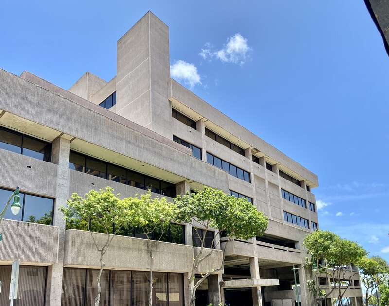 Built in 1960, this Brutalist building was constructed as the headquarters of the Hawaii National Bank.  The building features a rough textured concrete exterior, boxy geometric forms, a protruding parapet on the exterior facing walls, ribbon