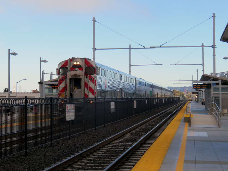 An inbound express train passing under newly installed catenary structures at San Bruno station in July 2018