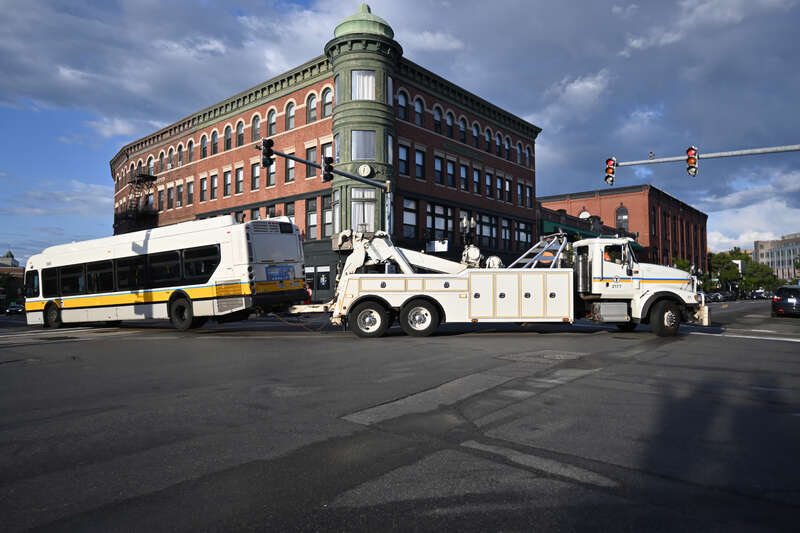 A disabled MBTA New Flyer XDE40 bus is towed away in Brighton Center, MA.