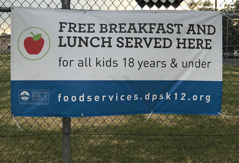 A sign that reads &quot;Free Breakfast and Lunch Served Here for all kids 18 years and younger&quot; hanging on a fence at West High School in Denver.