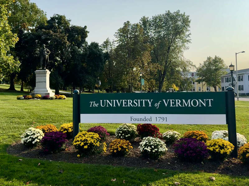 A photograph of the University of Vermont sign on the University Green, with a statue of Marquis de Lafayette in the background. Located on the University of Vermont campus in Burlington, Vermont.