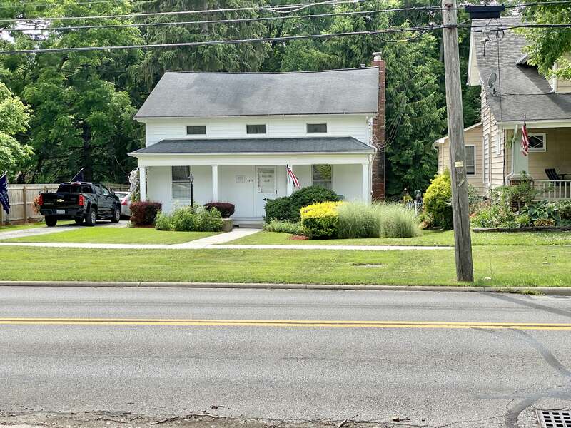 Built in the mid-19th Century, this one-and-a-half-story Greek Revival-style house features a wooden exterior with three small attic windows on the front facade, six-over-six double-hung windows, a mid-20th Century front door, a porch with square