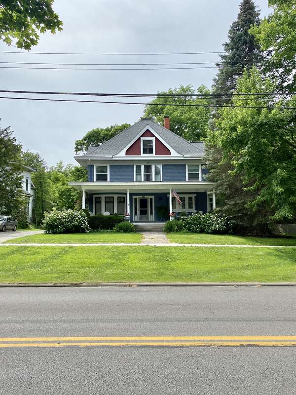Built around the turn of the 20th Century, this Queen Anne-style house features a shingle and clapboard exterior with a hipped roof featuring a flared lower portion and broad overhanging eaves, stucco-clad gables on the front and side facades,