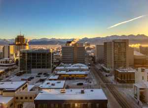 The sun sets on Downtown Anchorage on a cold, quiet day in February, with the Chugach Mountain Range just below the horizon above snow-covered rooftops, as seen from the Hotel Captain Cook.