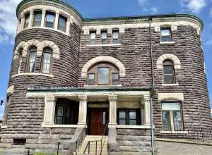 Built in 1889, this Richardsonian Romanesque Revival-style building was designed by Joseph W. Yost to serve as the jail and Sheriff’s residence for Licking County, Ohio.  The building features a rusticated brownstone exterior with limestone trim, a